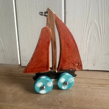 Load image into Gallery viewer, Small sailboat model with a brown sail and turquoise wheels on a wooden surface.