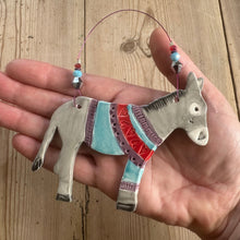 Load image into Gallery viewer, Hand holding a decorative donkey ornament with colourful patterned jumper on a wooden surface