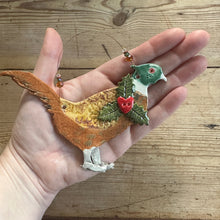 Load image into Gallery viewer, Hand holding a decorative pheasant ornament with holly leaves and berries on a wooden surface