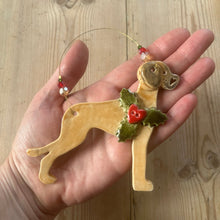 Load image into Gallery viewer, Hand holding a dog-shaped Christmas ornament with holly on a wooden surface