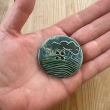 Load image into Gallery viewer, Hand holding a green ceramic button with wave design on a wooden surface