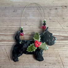 Load image into Gallery viewer, Black dog-shaped ornament with holly leaves and a heart shaped berry on a wooden surface