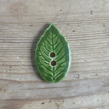 Load image into Gallery viewer, Green ceramic leaf-shaped button on a wooden surface

