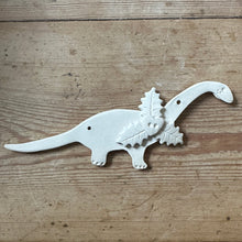 Load image into Gallery viewer, White dinosaur-shaped decoration awaiting glaze on a wooden surface
