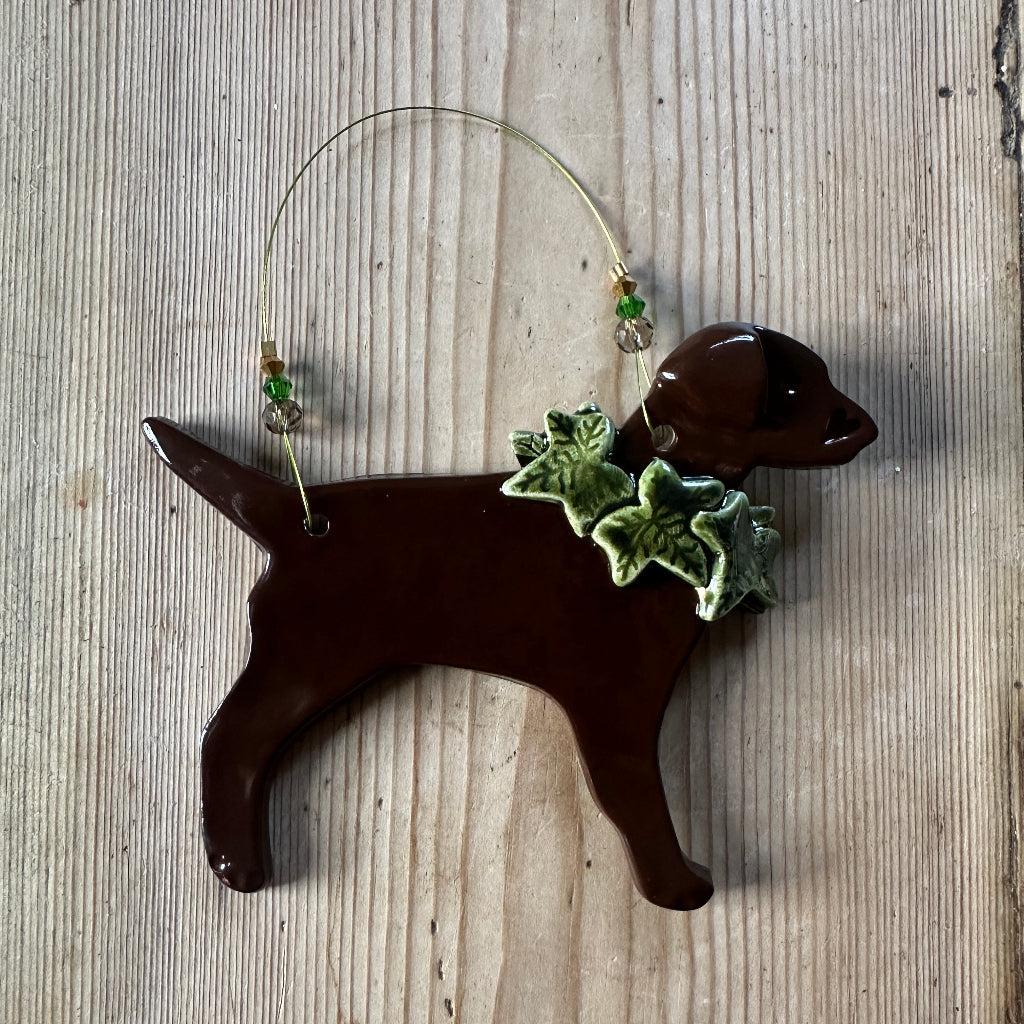 Decorative dog decoration with holly around its neck on a wooden surface