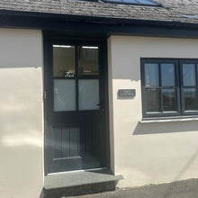 Load image into Gallery viewer, Cottage entrance with a door and window on a clear day
