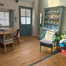 Load image into Gallery viewer, Living room with wooden floor, dining table, and shelves with decorative items.
