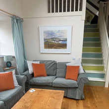 Load image into Gallery viewer, Living room with gray sofa, wooden coffee table, and staircase with colorful steps.
