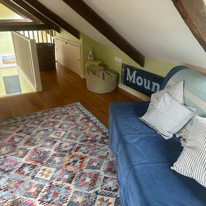 Mezzanine with blue sofa, patterned rug, and wooden beams on the ceiling.