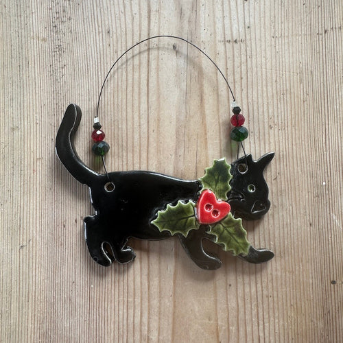 Decorative black cat ornament with holly and a red heart on a wooden surface