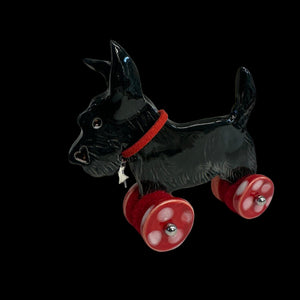 Black ceramic dog figurine with red wheels on a light  background