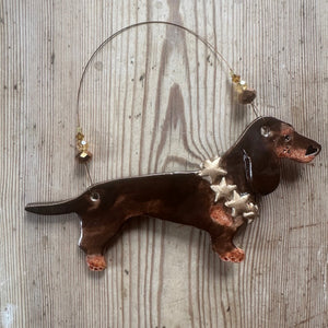 Decorative ceramic dachshund ornament with stars around its neck on a wooden surface