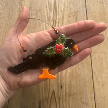 Load image into Gallery viewer, Hand holding a small decorative item resembling a bird with holly leaves and berries on a wooden surface.
