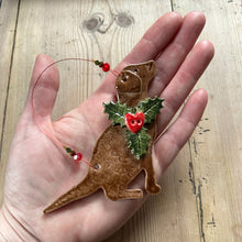Load image into Gallery viewer, Hand holding a dog shaped ornament with holly leaves and berries on a wooden surface
