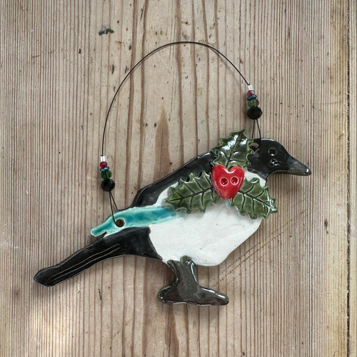 Decorative magpie ornament with holly on a wooden surface