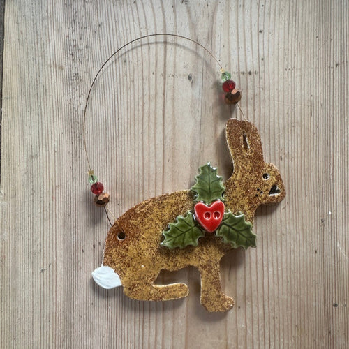 Decorative rabbit ornament with holly leaves and berries on a wooden surface