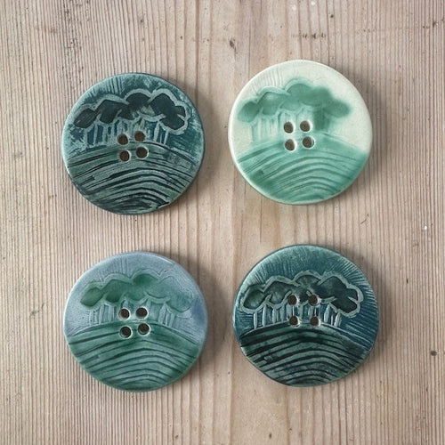 Four green ceramic buttons with a landscape design on a wooden surface