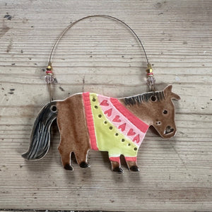 Decorative horse ornament with a colourful jumper on a wooden surface