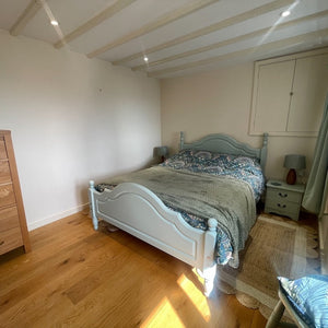 Bedroom with wooden drawers, bed, and 2 windows with curtains and blinds.