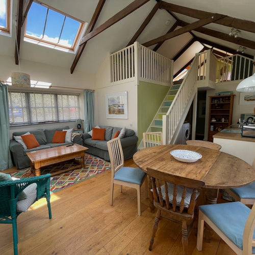 Living room with wooden floor, rug, coffee table, green grey sofa, and a round wooden dining table.