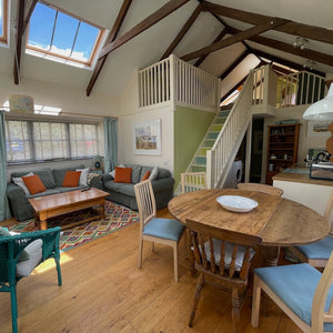 Living room with wooden floor, greeny grey sofa, and a round wooden table.