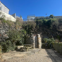 Load image into Gallery viewer, Parking and patio area with stone wall and bench on a sunny day
