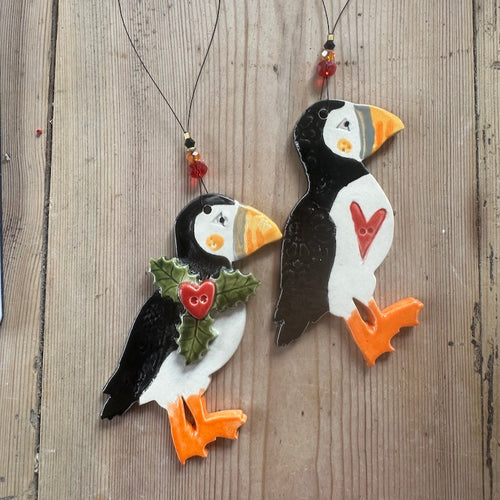 Two decorative puffin figures with heart and holly designs on a wooden surface
