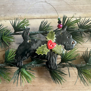 Decorative wall hanging with black dog figures and greenery on a wooden surface