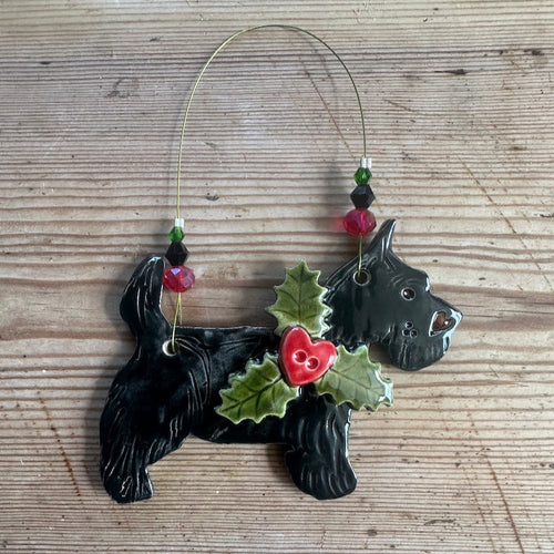 Black dog-shaped ornament with holly leaves and a heart shaped berry on a wooden surface