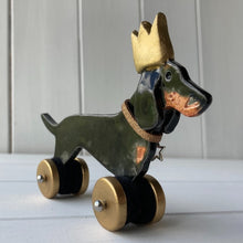 Load image into Gallery viewer, Dachshund dog ornament on wheels with a gold party hat.
